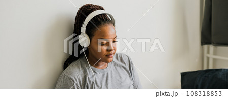 Banner smiling young african woman listening to music with headphones while relaxing on bed at home, meditating. Copy space and empty space for text Banner smiling young african woman listening to music with headphones while relaxing on bed at home, meditating. Copy space and empty space for text 108318853