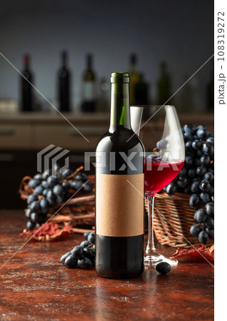 Bottle and glass of red wine with blue grapes on a vintage table. Bottle and glass of red wine with blue grapes on a vintage table. 108319272