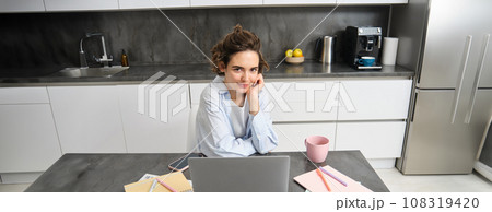 Image of young working woman, looking at laptop, sitting at home and watching webinar, connecting to team meeting, studying indoors Image of young working woman, looking at laptop, sitting at home and watching webinar, connecting to team meeting, studying indoors 108319420