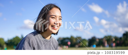 Vertical shot of happy korean girl sitting in park, learning how to play ukulele, singing and relaxing 108319599