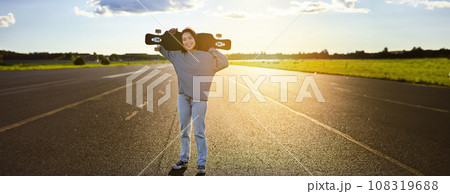 Young asian woman standing with longboard on sunny road, skating in skate park on her cruiser Young asian woman standing with longboard on sunny road, skating in skate park on her cruiser 108319688
