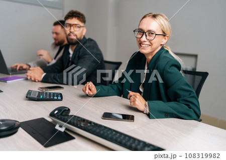 Portrait of cheerful businesswoman in suit laughing at funny joke with young coworkers in office. Friendly work team enjoying positive emotions together. Happy colleagues staff group having fun 108319982