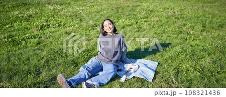 Young asian girl enjoying sunny day outdoors. Happy student having picnic on grass in park, playing ukulele 108321436