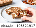 hand holding a slice of almond butter whole grain toast over a white plate 108321917
