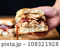 hand holding sandwich filled with alabama chicken and white bbq sauce 108321928
