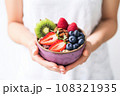 hand holding an acai bowl topped with fresh berries on a white table 108321935