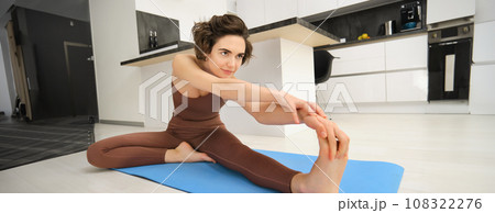Portrait of young healthy woman stretches her legs, leaning towards feet, warm-up, doing workout exercises at home in bright room 108322276