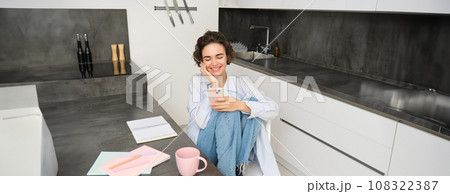 Beautiful girl with smartphone, sits at home, does homework, watches smth on mobile phone app 108322387