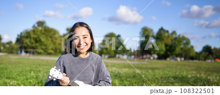 Positive hipster asian girl, playing ukulele and making faces, singing and feeling happy 108322501
