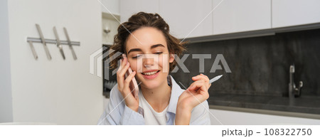Image of woman working from home, writing down information during a phone call, calling someone, using smartphone Image of woman working from home, writing down information during a phone call, calling someone, using smartphone 108322750
