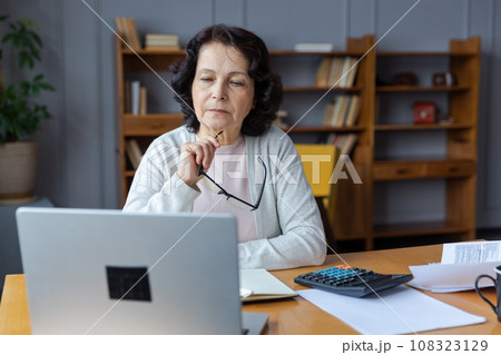 Confident stylish european middle aged senior woman using laptop at home. Stylish older mature 60s lady sitting at table looking at computer screen typing chatting reading writing email Confident stylish european middle aged senior woman using laptop at home. Stylish older mature 60s lady sitting at table looking at computer screen typing chatting reading writing email 108323129
