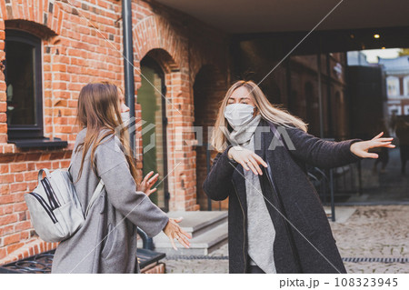 Two young stylish women in medical masks dancing and having fun while walking the street in town. Friends strolling outdoor in city Two young stylish women in medical masks dancing and having fun while walking the street in town. Friends strolling outdoor in city 108323945
