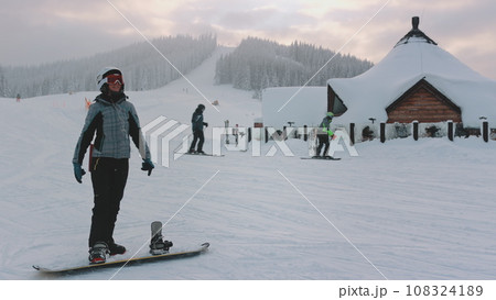 Woman enjoy winter holiday vacation on ski resort. Snowboard girl listen music, and have fun, ski slope, snow covered forest in background. Active sport. Bukovel, Carpathian mountains, Ukraine 108324189