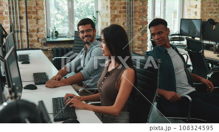 Project team. Group of cheerful young employees working on computers and talking with each other while sitting in modern open space Project team. Group of cheerful young employees working on computers and talking with each other while sitting in modern open space 108324595