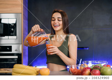 Young woman pouring fresh lemonade from jug into glass at home Young woman pouring fresh lemonade from jug into glass at home 108324960