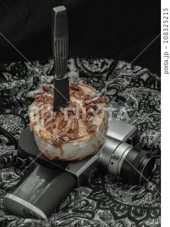 The black metal knife is inserted into the Caramel Pecan topped with caramel frosting and pecans on the old movie camera 8mm. The black metal knife is inserted into the Caramel Pecan topped with caramel frosting and pecans on the old movie camera 8mm. 108325215