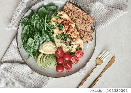 Scramble eggs with cherry tomatoes, fresh spinach leaves, avocado and crispbreads 108326098