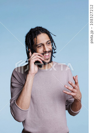 Cheerful arab man having fun conversation on smartphone and gestuculating with hand. Happy smiling person with carefree facial expression wearing casual clothes talking on mobile phone Cheerful arab man having fun conversation on smartphone and gestuculating with hand. Happy smiling person with carefree facial expression wearing casual clothes talking on mobile phone 108327212