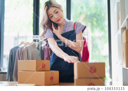 Starting small business entrepreneur of independent Asian female online seller talking on the phone with a customer and packing products for delivery to the customer. and SME delivery concept. Starting small business entrepreneur of independent Asian female online seller talking on the phone with a customer and packing products for delivery to the customer. and SME delivery concept. 108333115