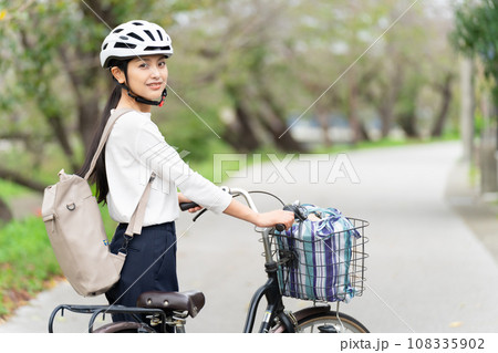 サイクリングヘルメットをかぶって自転車を引いて歩く若い女性 サイクリングヘルメットをかぶって自転車を引いて歩く若い女性 108335902