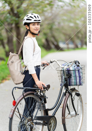 サイクリングヘルメットをかぶって自転車を引いて歩く若い女性 サイクリングヘルメットをかぶって自転車を引いて歩く若い女性 108335909