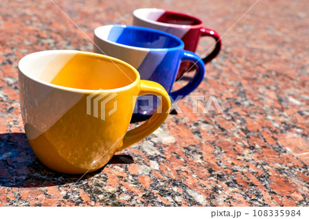 Time of ceremony for tea and coffee.Colorful cups on red marble surface Time of ceremony for tea and coffee.Colorful cups on red marble surface 108335984