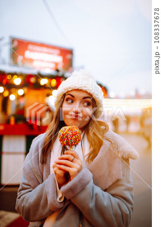 Young woman with caramel apple on Christmas market. Smiling woman in winter style clothes posing. 108337678