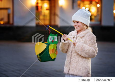 Little preschool kid girl holding selfmade traditional owl lanterns with candle for St. Martin procession. child happy about children and family parade in kindergarten. German tradition Martinsumzug 108338707