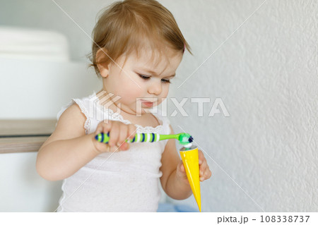 Little baby girl holding toothbrush and brushing first teeth. Toddler learning to clean milk tooth. Prevention, hygiene and healthcare concept. Happy child in bathroom Little baby girl holding toothbrush and brushing first teeth. Toddler learning to clean milk tooth. Prevention, hygiene and healthcare concept. Happy child in bathroom 108338737