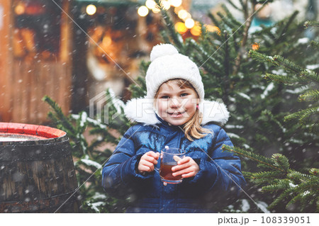 Little cute preschool girl drinking hot children punch or chocolate on German Christmas market. Happy child on traditional family market in Germany, Laughing boy in colorful winter clothes Little cute preschool girl drinking hot children punch or chocolate on German Christmas market. Happy child on traditional family market in Germany, Laughing boy in colorful winter clothes 108339051