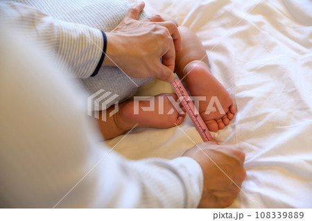 赤ちゃんの成長を確かめる父親　メジャーで足裏のサイズを測る　乳幼児　イクメン　育児休暇　0歳乳幼児 108339889