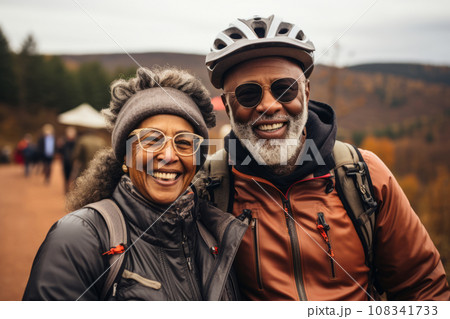 An elderly African American couple rides bicycles, enjoying the mountain landscape, man and woman wearing a helmet, healthy lifestyle concept. 108341733