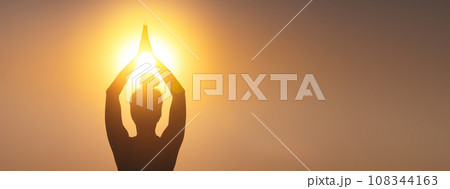 silhouette of a woman raising her hands, praying for God's blessings in the light of sunset or sunrise, practicing yoga and meditation in nature, concept of religion, freedom and spirituality 108344163