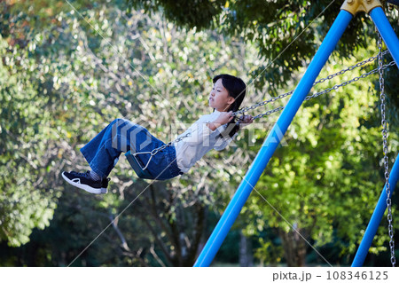 秋の公園でブランコを遊んでいる小学生の女の子の様子 108346125