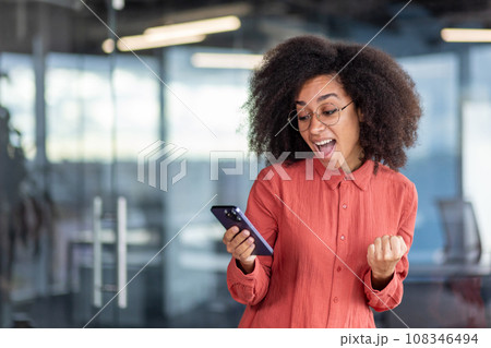 Young successful businesswoman boss received online notification on phone victory, good results of achievement, woman celebrates victory and triumph, happy holds smartphone in hands, uses app. Young successful businesswoman boss received online notification on phone victory, good results of achievement, woman celebrates victory and triumph, happy holds smartphone in hands, uses app. 108346494