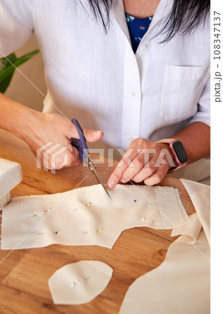 Seamstress cutting beige fabric with scissors. 108347137