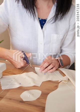 Seamstress cutting beige fabric with scissors. 108347138