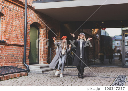 Millennial young women having fun and dance on city street. Female funny friends enjoying autumn day around the city. 108347257