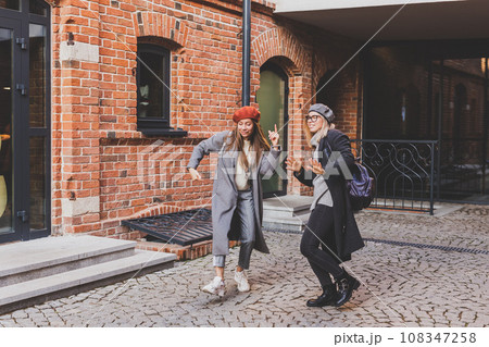 Millennial young women having fun and dance on city street. Female funny friends enjoying autumn day around the city. 108347258
