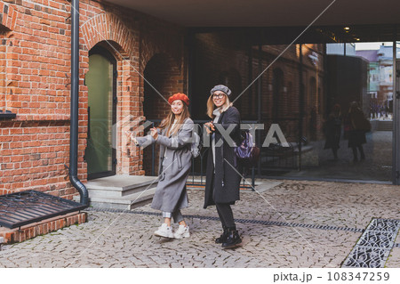 Millennial young women having fun and dance on city street. Female funny friends enjoying autumn day around the city. 108347259