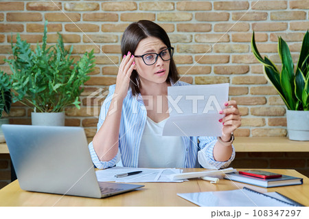 Young business woman with paper letter sitting at desk with computer in office 108347297