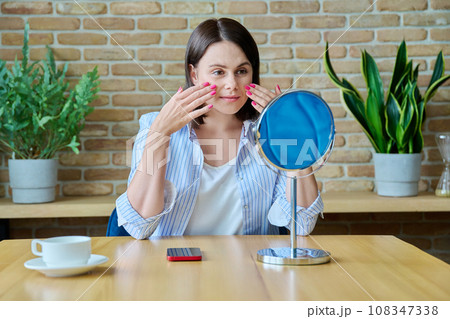 Young happy brunette looking at her face in mirror 108347338