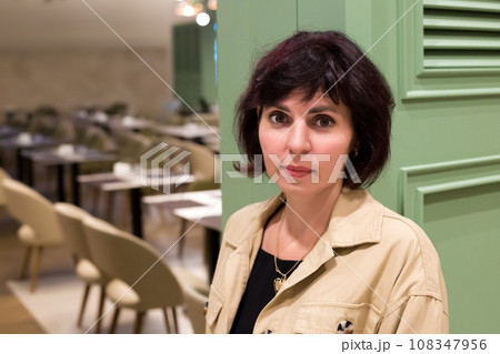 A woman stands at the green door of a large restaurant A woman stands at the green door of a large restaurant 108347956