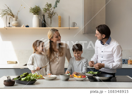 Cheerful couple of parents and two kids cooking fresh food Cheerful couple of parents and two kids cooking fresh food 108348915