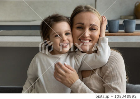 Cheerful mom with toothy smile cuddling happy daughter kid 108348995