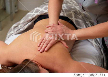 Massagist performing back massage to female client. 108349441