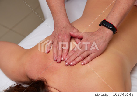 Massagist performing back massage to female client. 108349545