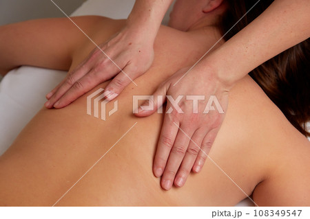 Massagist performing back massage to female client. 108349547