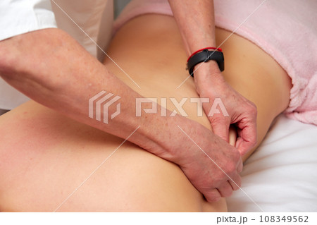Massagist performing back massage to female client. Massagist performing back massage to female client. 108349562