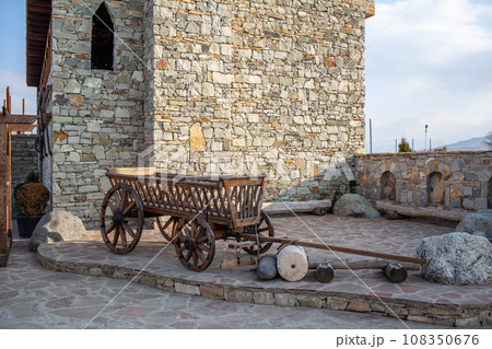 Close-up of an old wooden cart made from logs, used to transport goods, crops or savagery, next to a high stone wall and a stone fence on a sunny summer day in Dagestan. Close-up of an old wooden cart made from logs, used to transport goods, crops or savagery, next to a high stone wall and a stone fence on a sunny summer day in Dagestan. 108350676